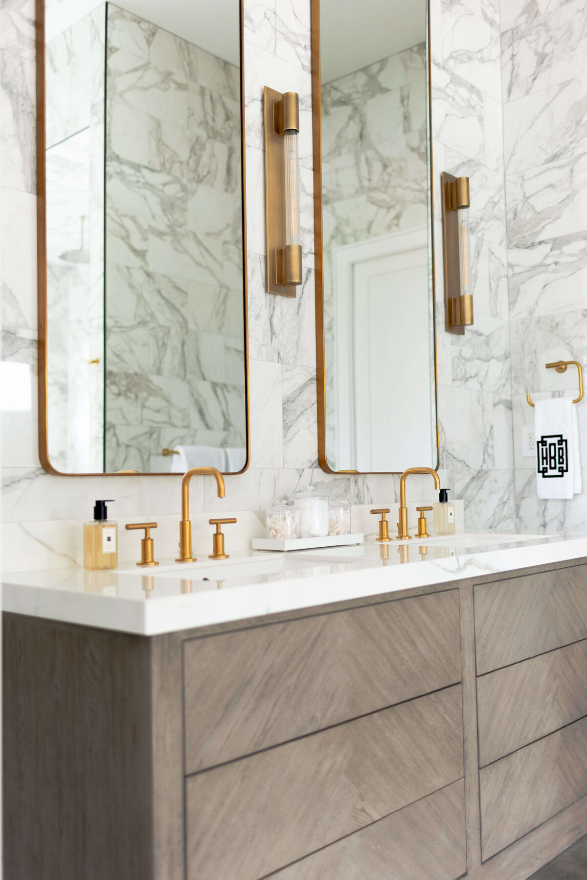 oyster creek studios building belt new build double wooden vanity with marble counters and gold hardware in bathroom with marble walls