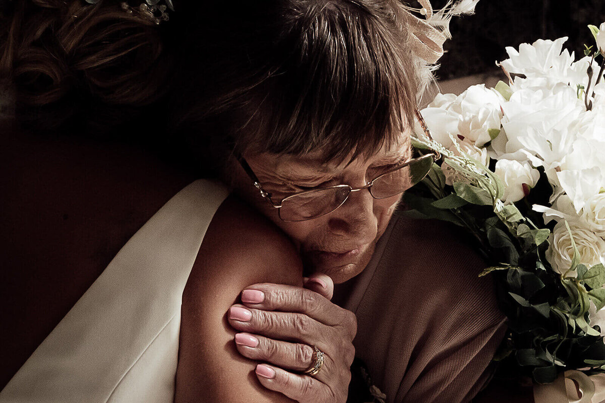 A gran holds her granddaughter bride tightly. The image focuses on the emotion in the grans face, eyes and hand.