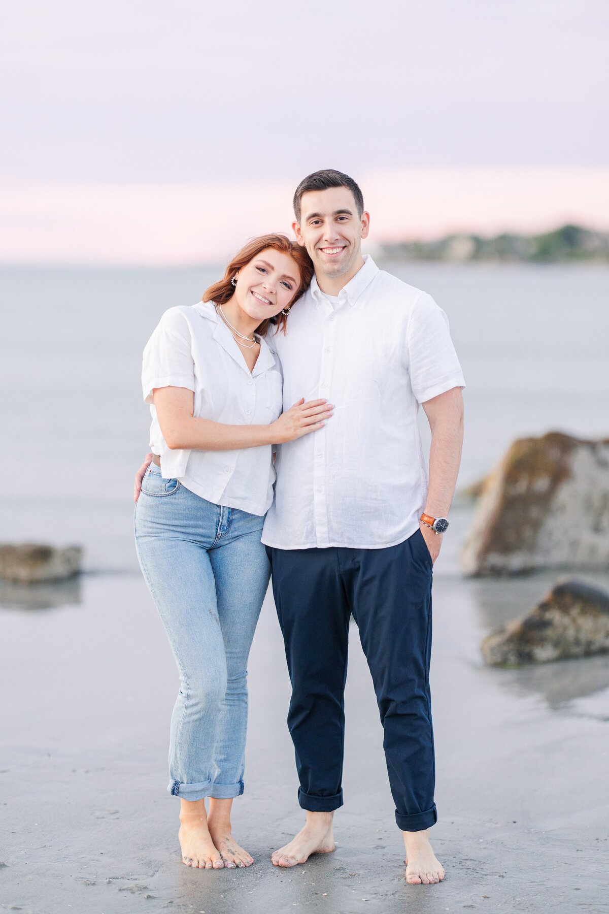 A couple standing side by side snuggled together during their Boston engagement session at Wingaersheek Beach.