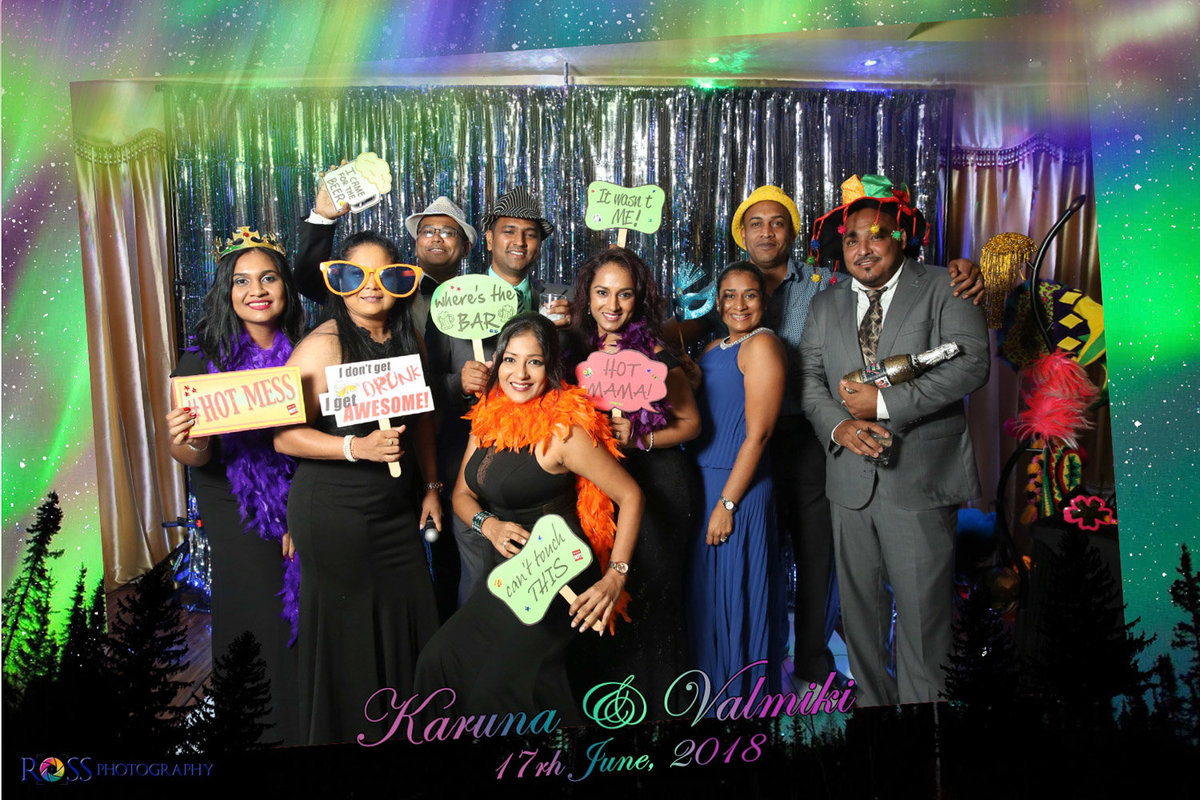 A large group of men and women stand ing front of silver curtain holding and wearing fun props. Photobooth by Ross Photography, Trinidad, W.I..