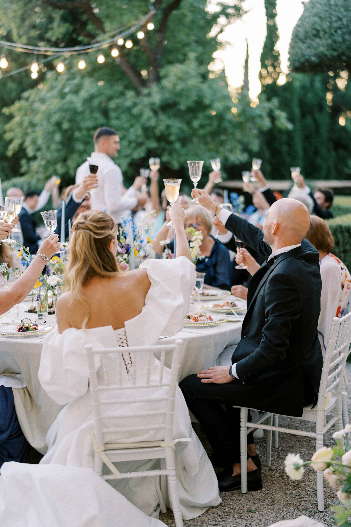 Candid moment of guests raising glasses during an outdoor wedding dinner celebration, captured by Toronto wedding photographer Nadtochiy