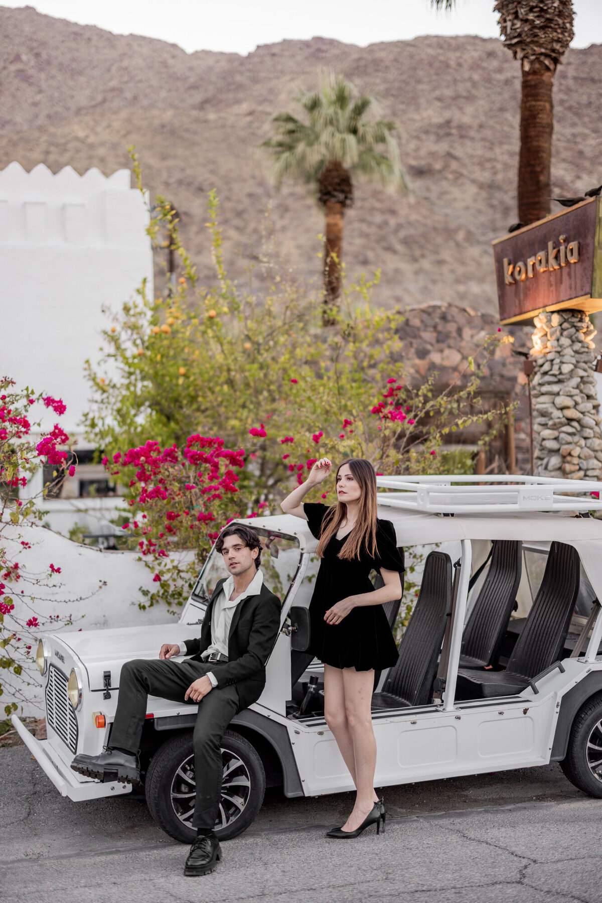 Couple sitting in a vintage convertible, surrounded by blooming florals and mid-century Palm Springs design.