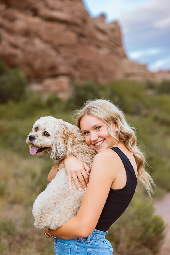 Girl and dog from behind, with red rocks in background.