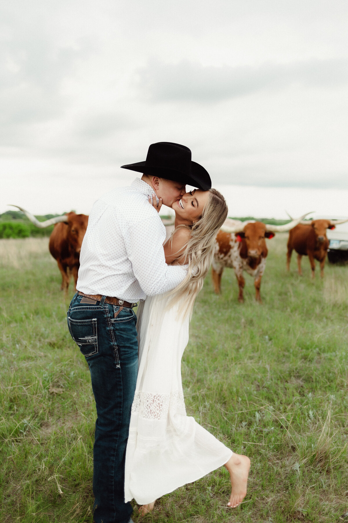 Kansas Wedding| Country Wedding Ideas| Bulls at The Wedding| Country Bride and Groom| Bride and groom dancing and laughing in front of heard of bulls during their wedding .
