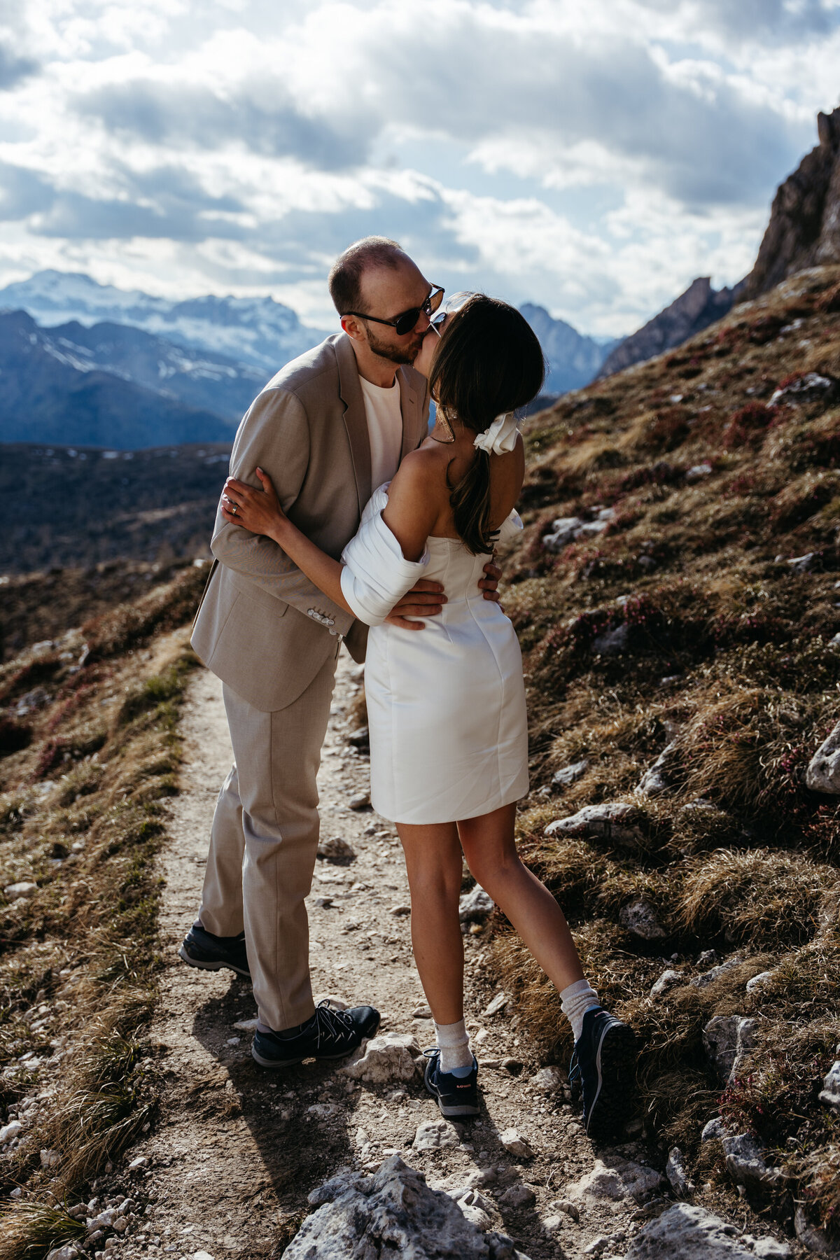 Groom kissing bride on alpine trail in Dolomites