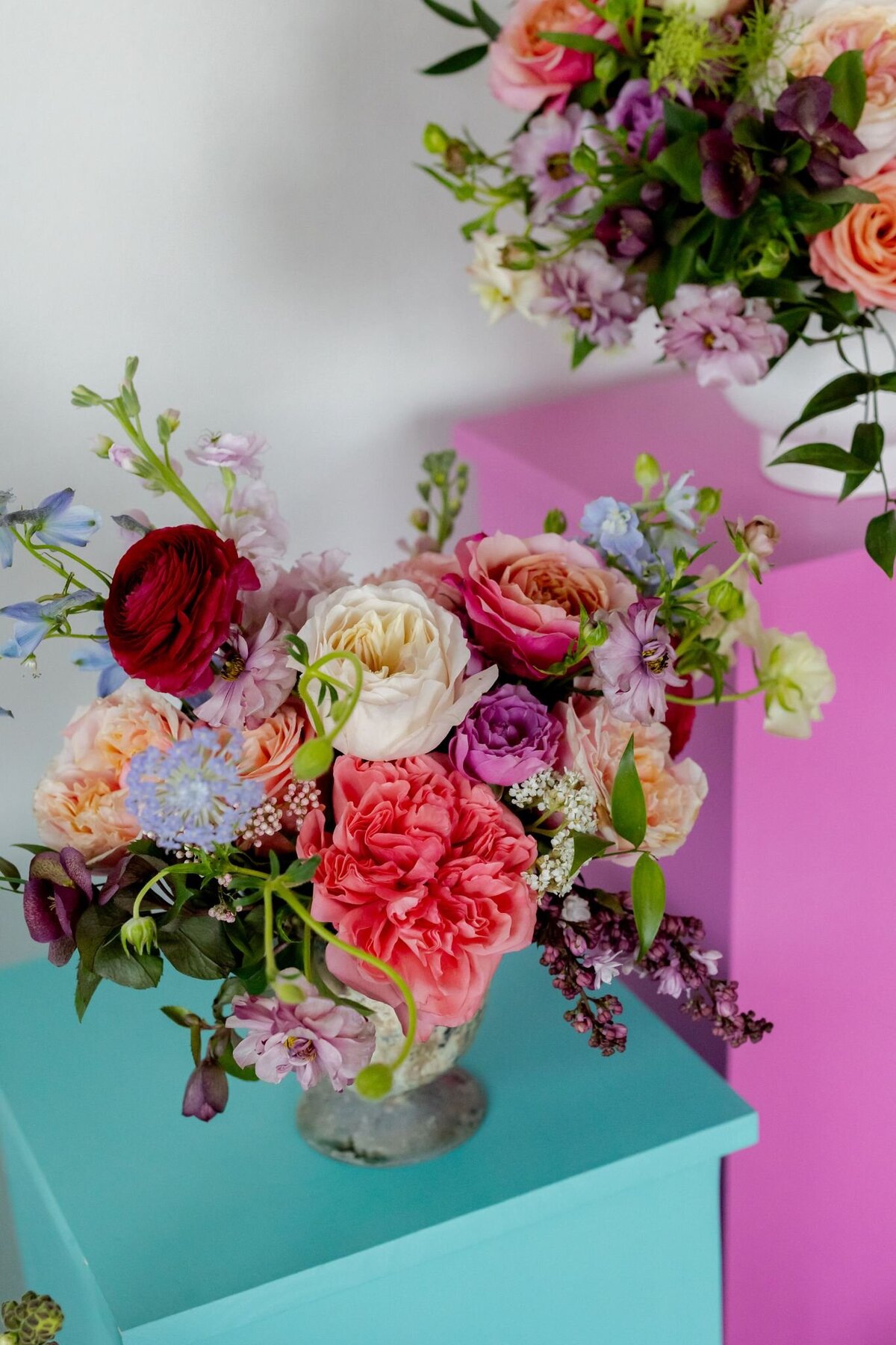 Colorful floral arrangement with roses, ranunculus, and garden blooms styled against pink and teal blocks by Tamara Menges Designs.