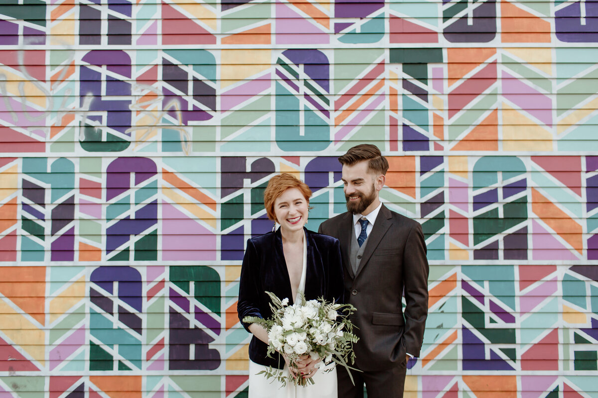 An urban Seattle wedding with bride and groom laughing in front of a colorful graffiti wall. Captured by Fort Worth wedding photographer, Megan Christine Studio