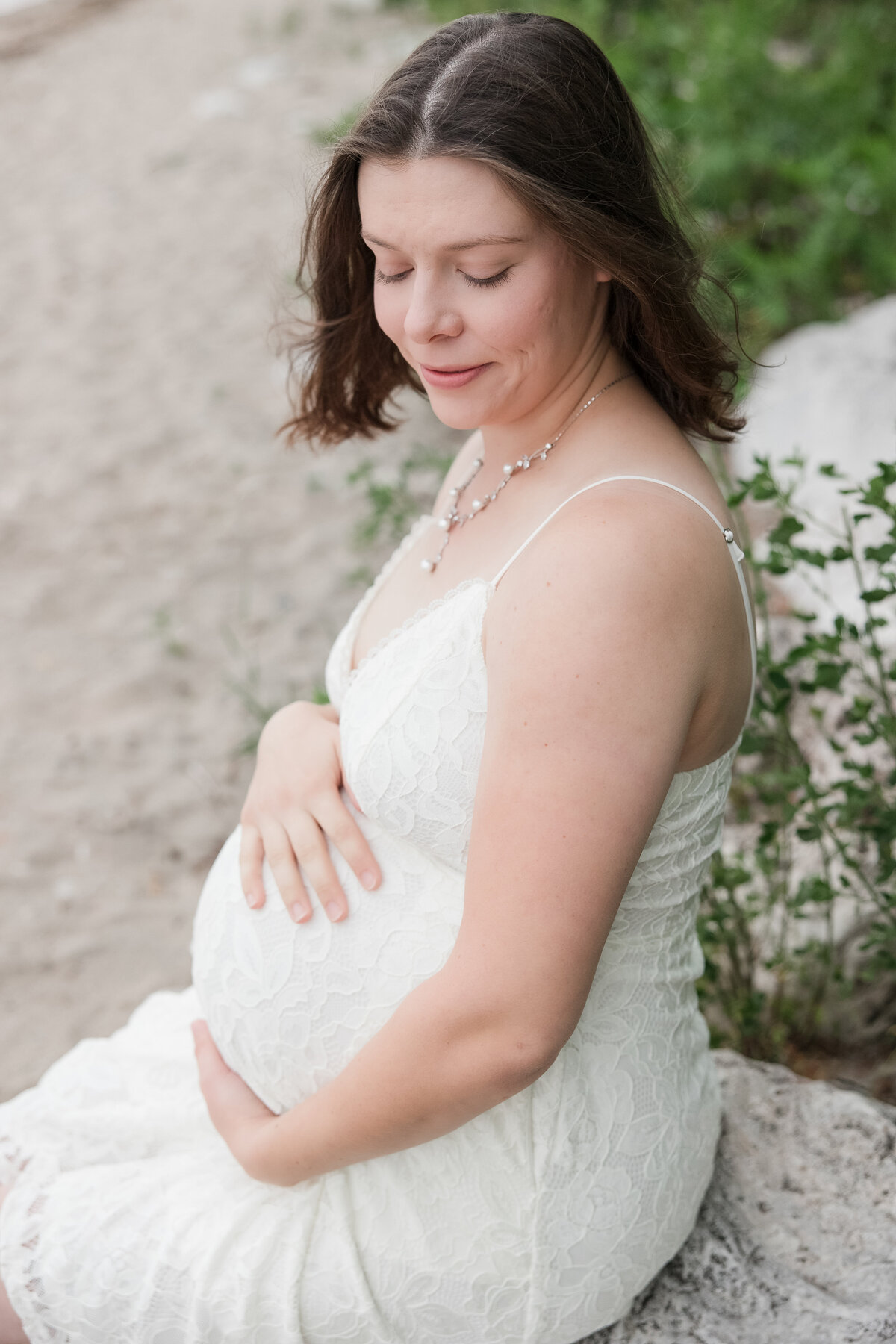 Expectant mother looking down her shoulder while seated on a rock