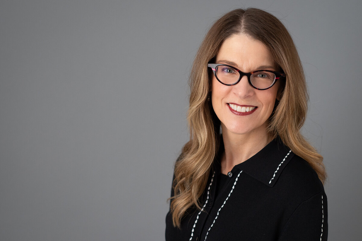 corporate headshot of smiling female on grey backdrop with glasses