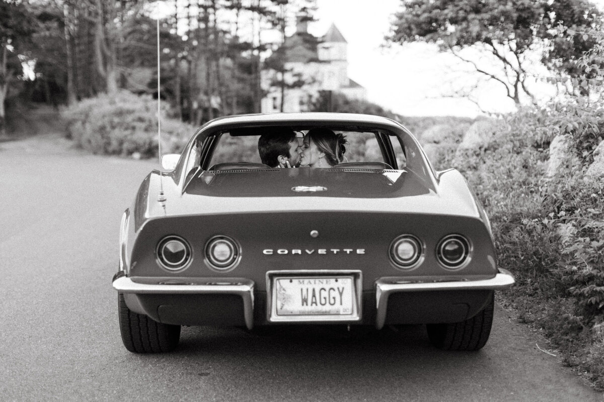 A guy and a girl are sitting in an old corvette and kissing.