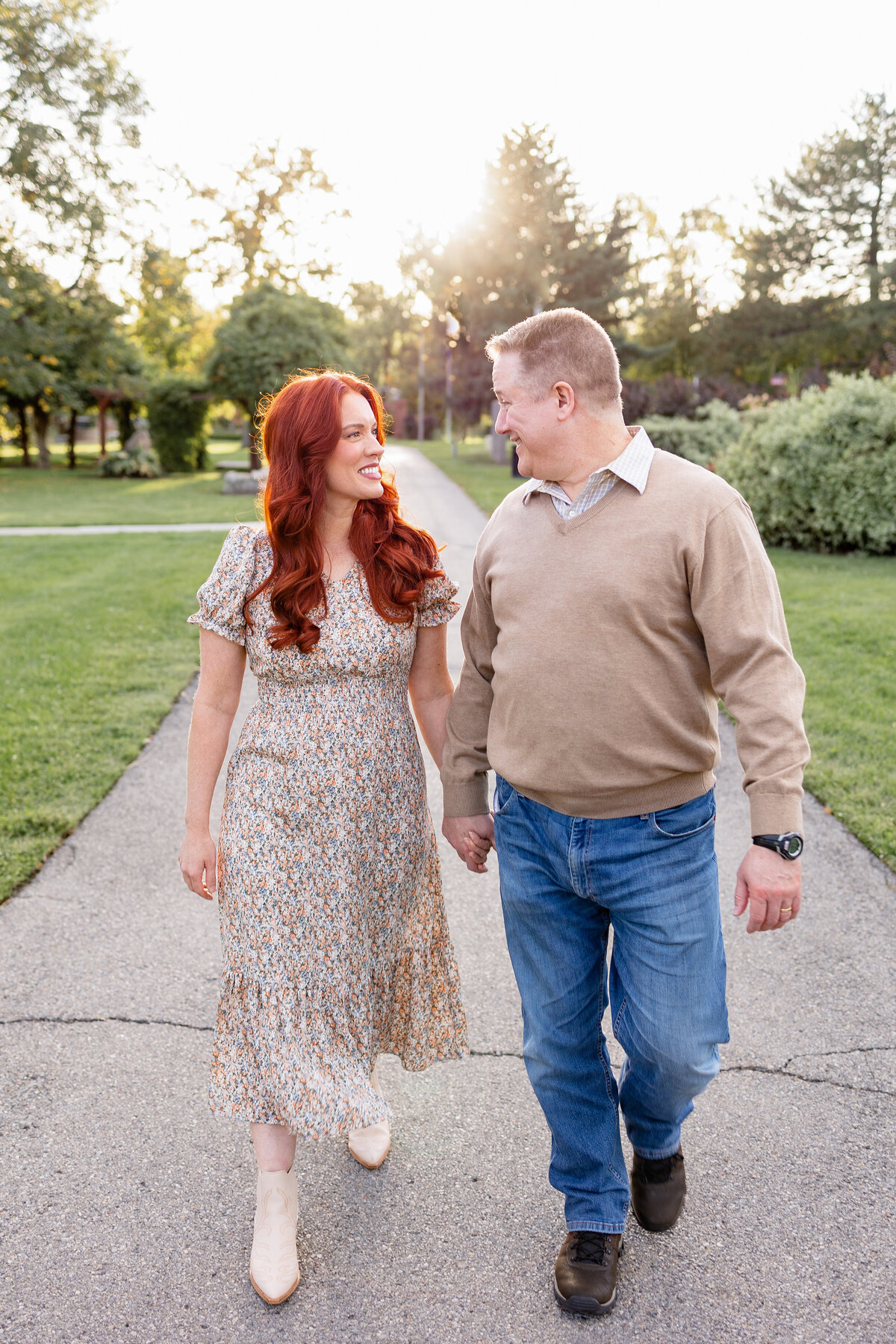 A loving couple walks hand in hand, gazing at each other with warm smiles as the sun sets behind them.