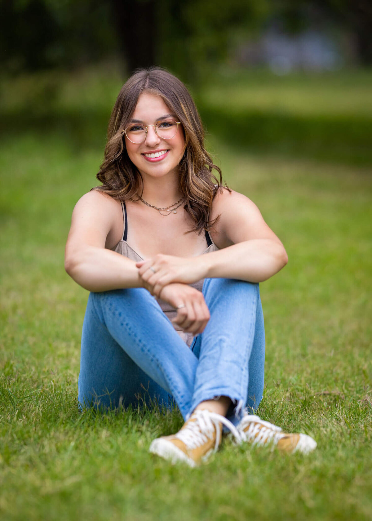 teenage girl wearing a tank top and jeans sitting in a grassy field