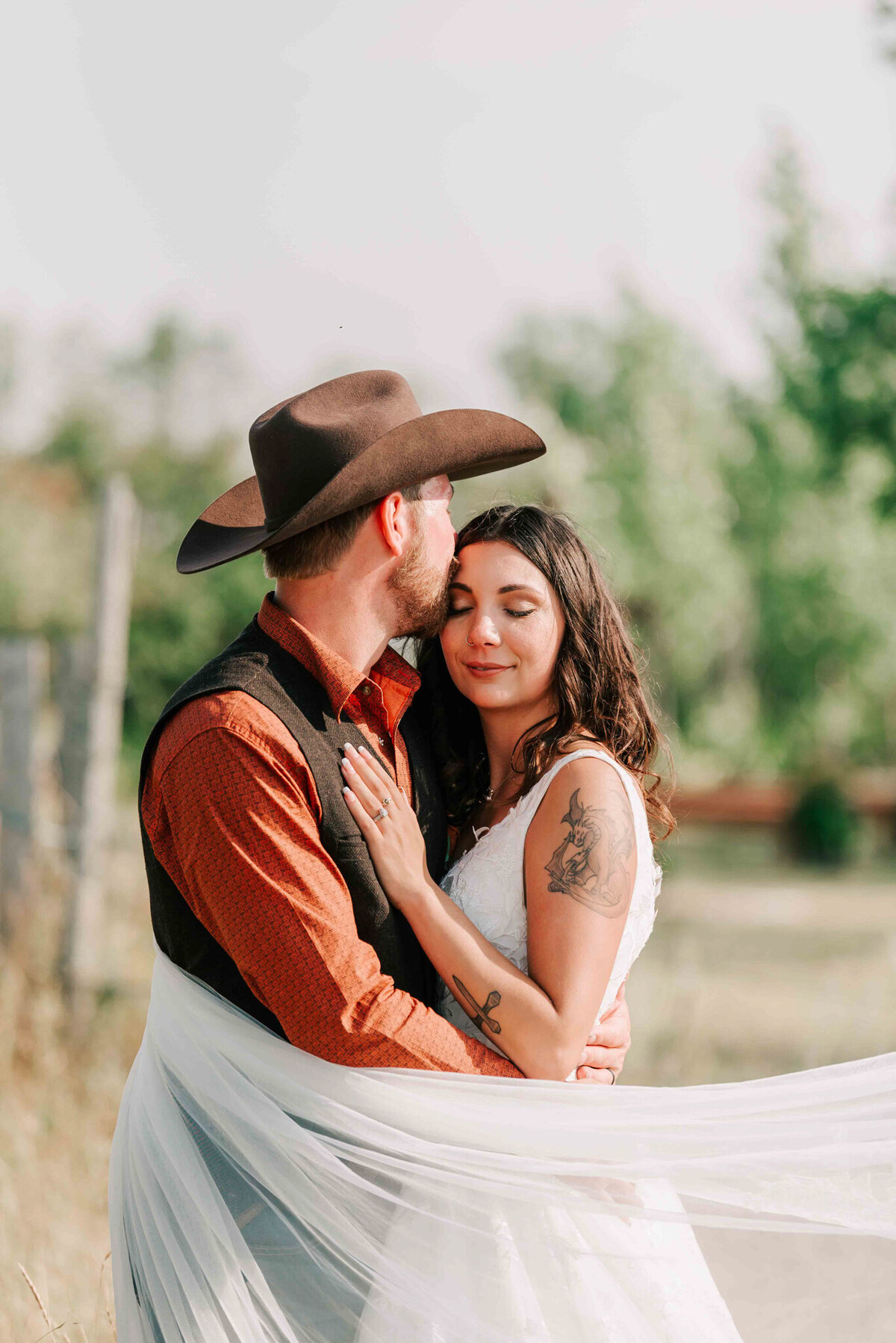 Groom kissing the brides forehead. Bride and groom are wrapped  up in the veil. Captured by Amanda Jordan Photography.