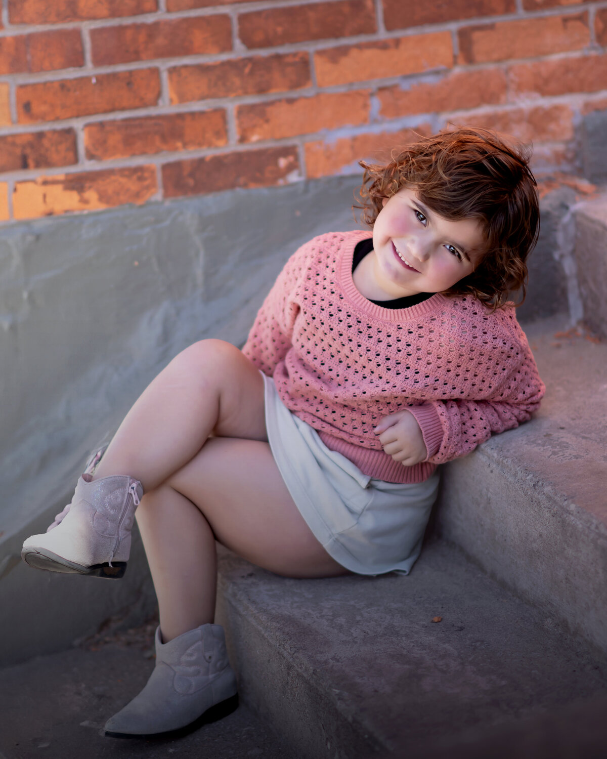 Girl sits on steps with her legs crossed wearing a pink sweater