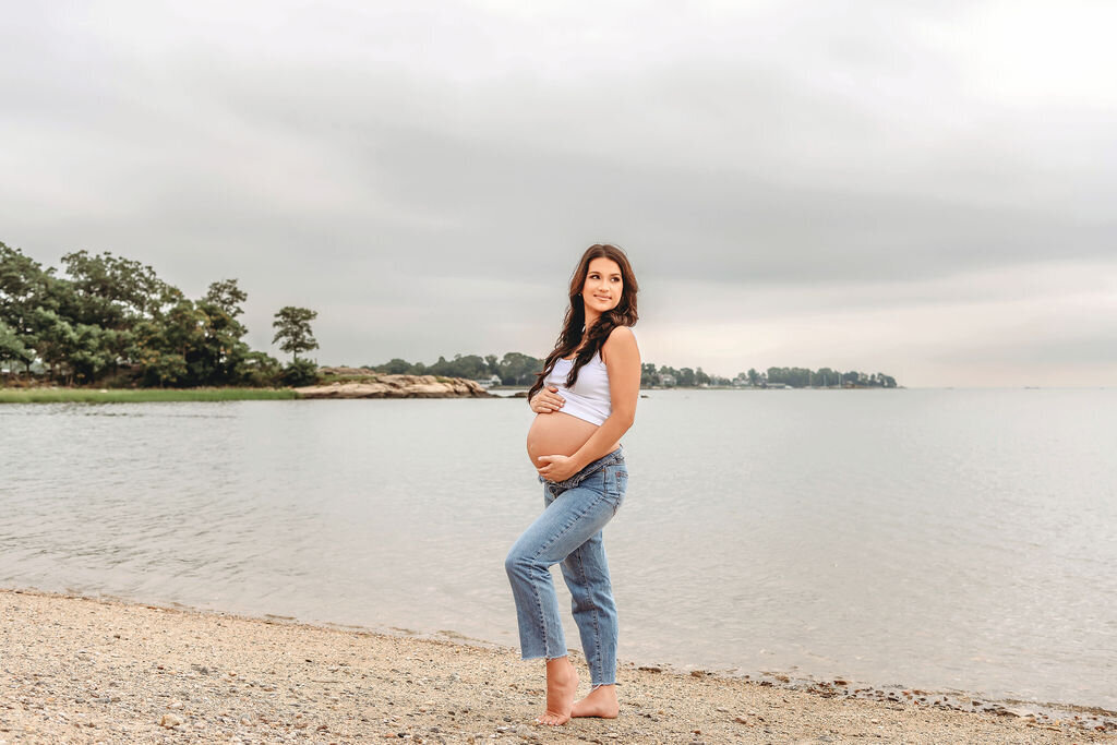 Casual maternity portrait of pregnant woman in white tank and jeans at waterfront