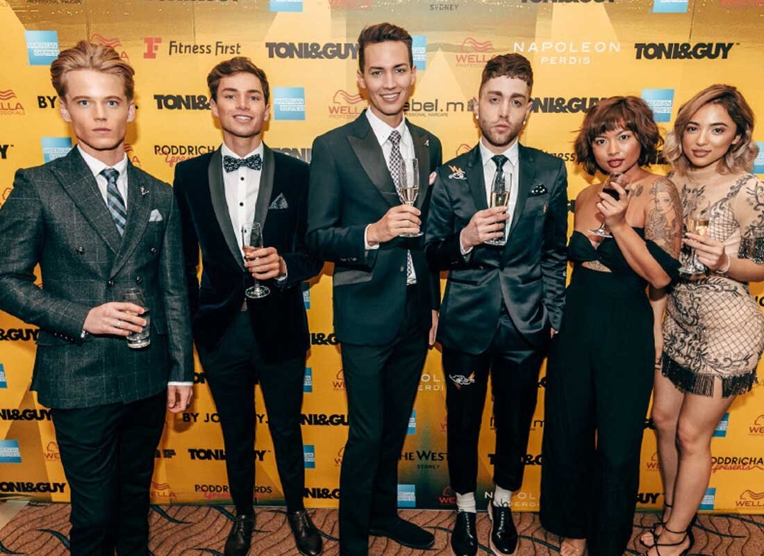 Well-dressed attendees posing with champagne in front of Toni & Guy branded media wall at fashion industry event