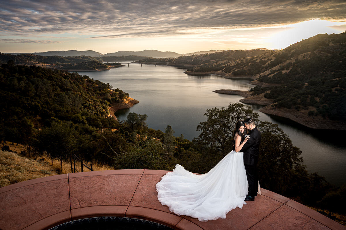A breathtaking wedding portrait of a bride and groom at Airla Road Vineyard, overlooking the Sierra Nevada foothills and a sparkling reservoir below, capturing the romance of Northern California wine country.