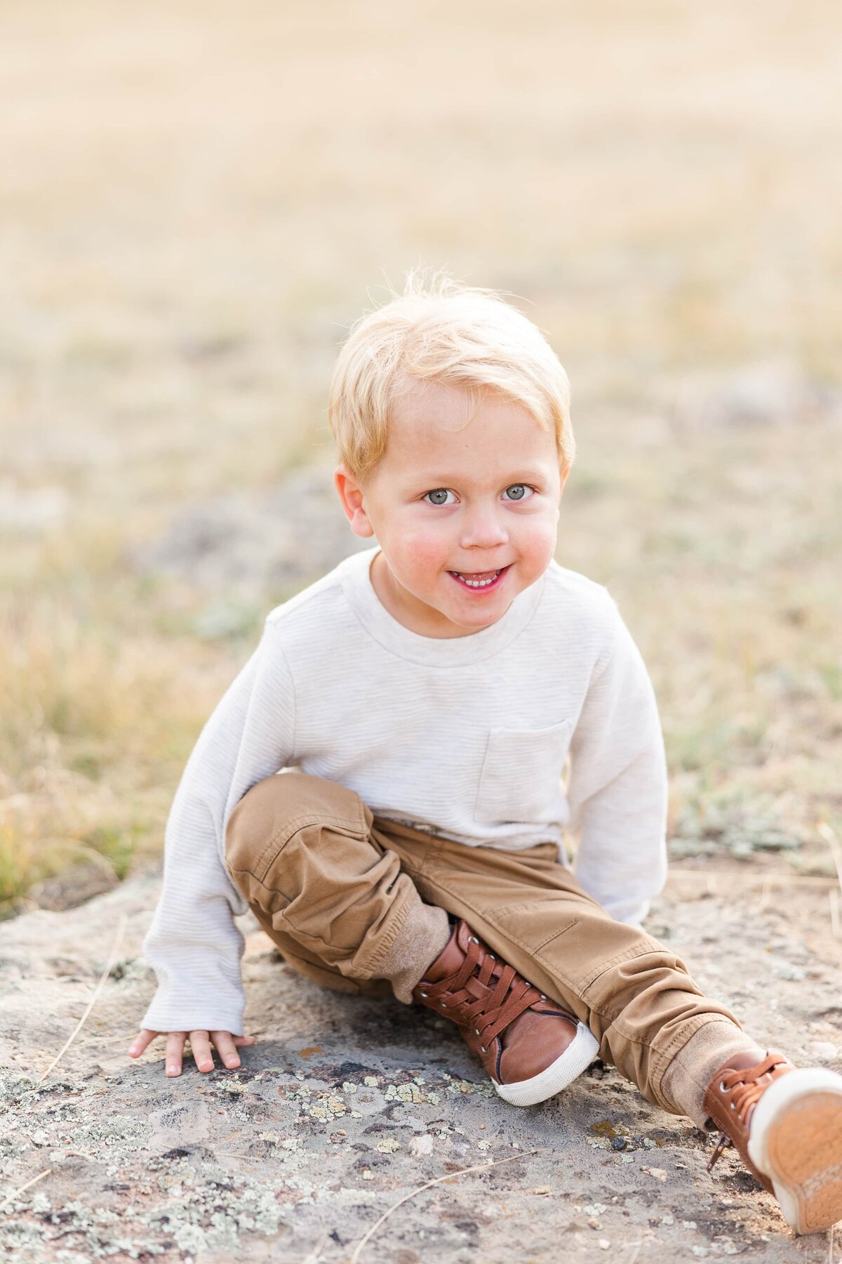 Toddler smiling at camera while sitting on a rock
