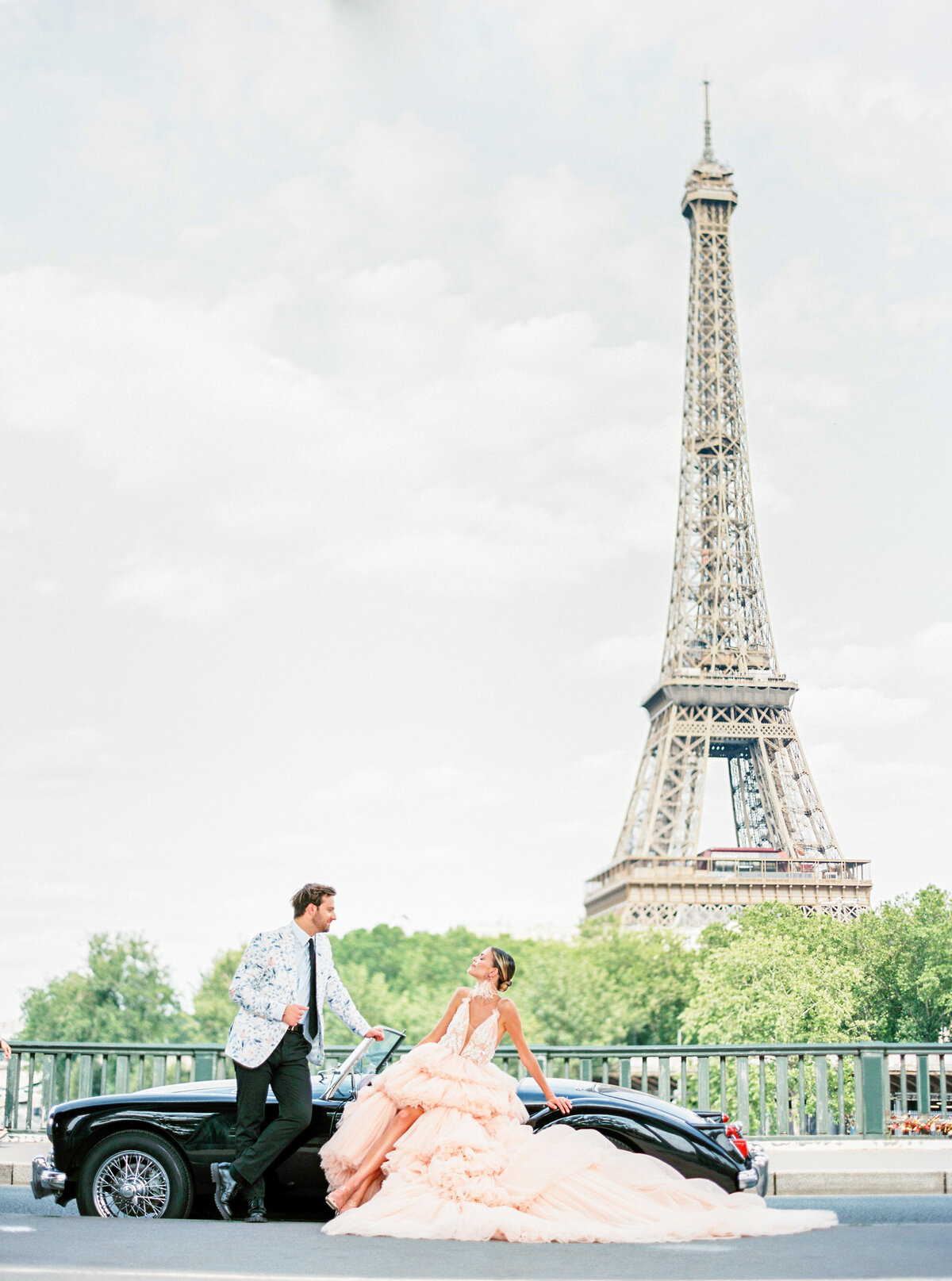 Paris Engagement session with bride in high low DPP peach hi-lo gown with long train, groom in a white and floral jacket with black vintage convertible with Eiffel Tower in the background photographed by Italy wedding photographer