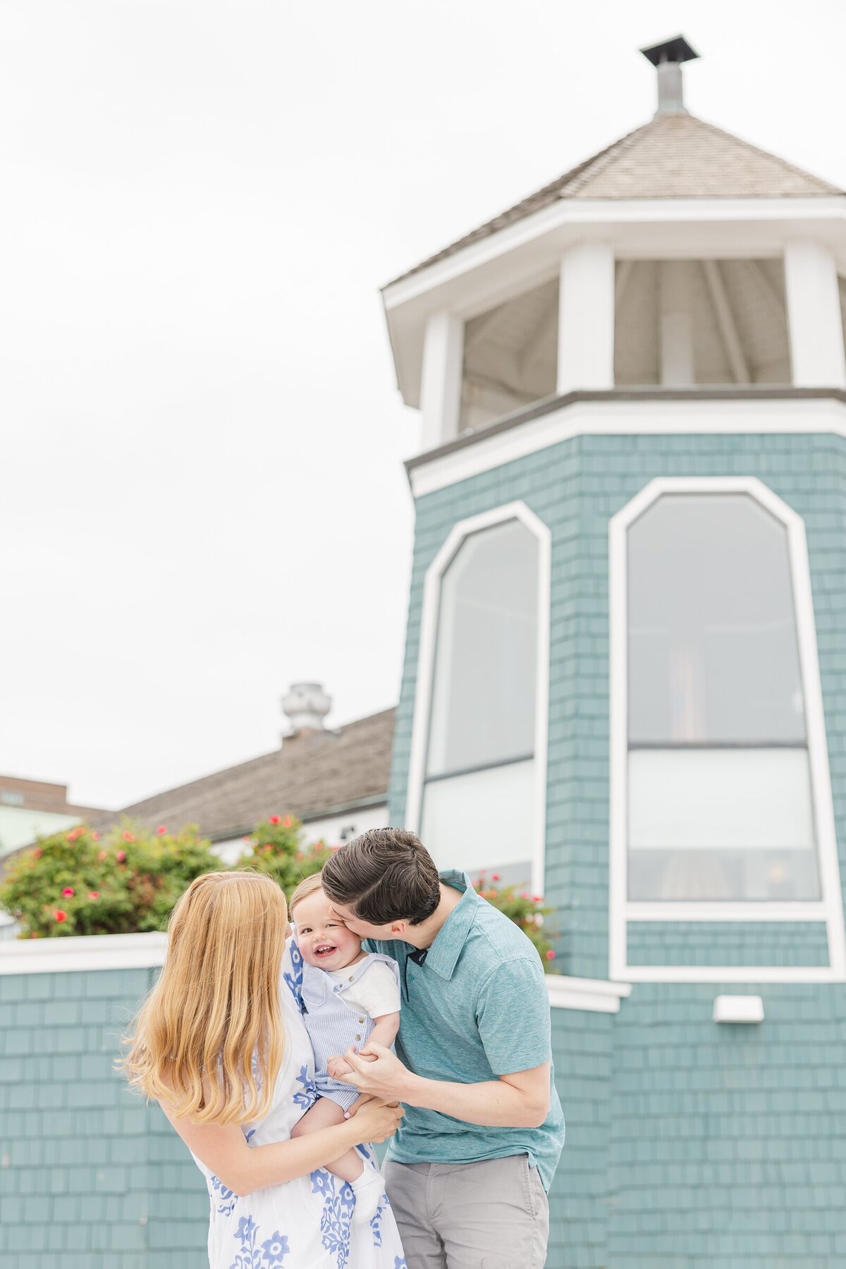 Parents kissing their toddler boy in front of a blue lighthouse by a Dayton family photographer