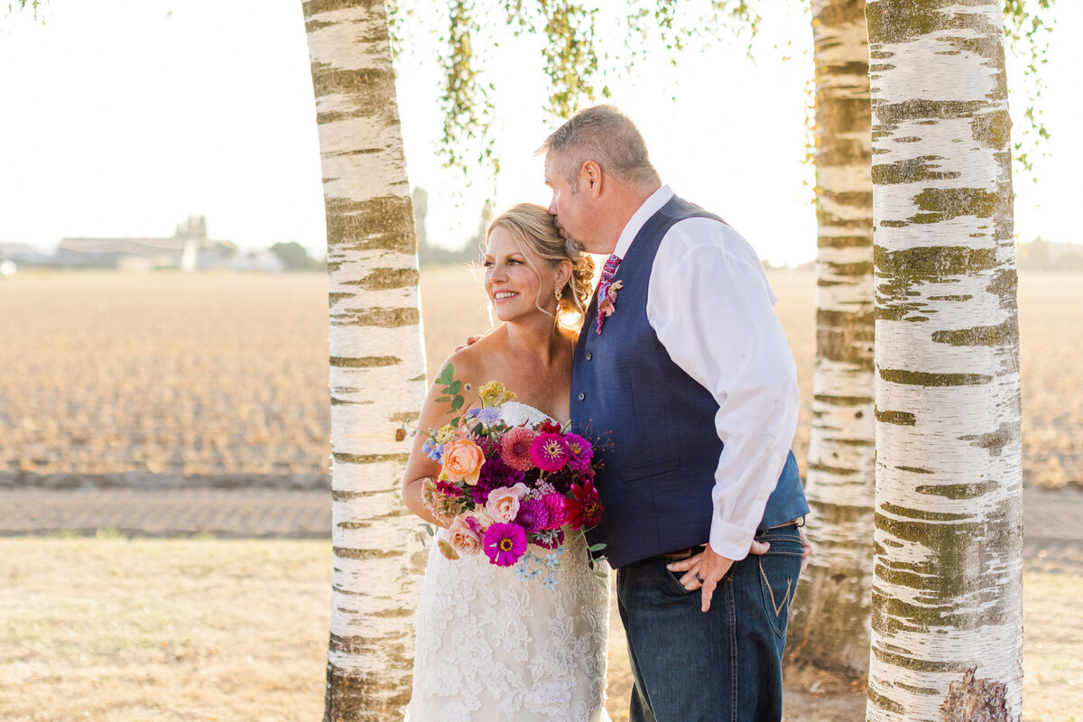 Bride-and-groom-kiss-under-large-birch-tree-at-beautiful-outdoor-venue-in-Skagit-County-at-Salt-Barn-in-Mount-Vernon-WA-photo-by-Joanna-Monger-Photography