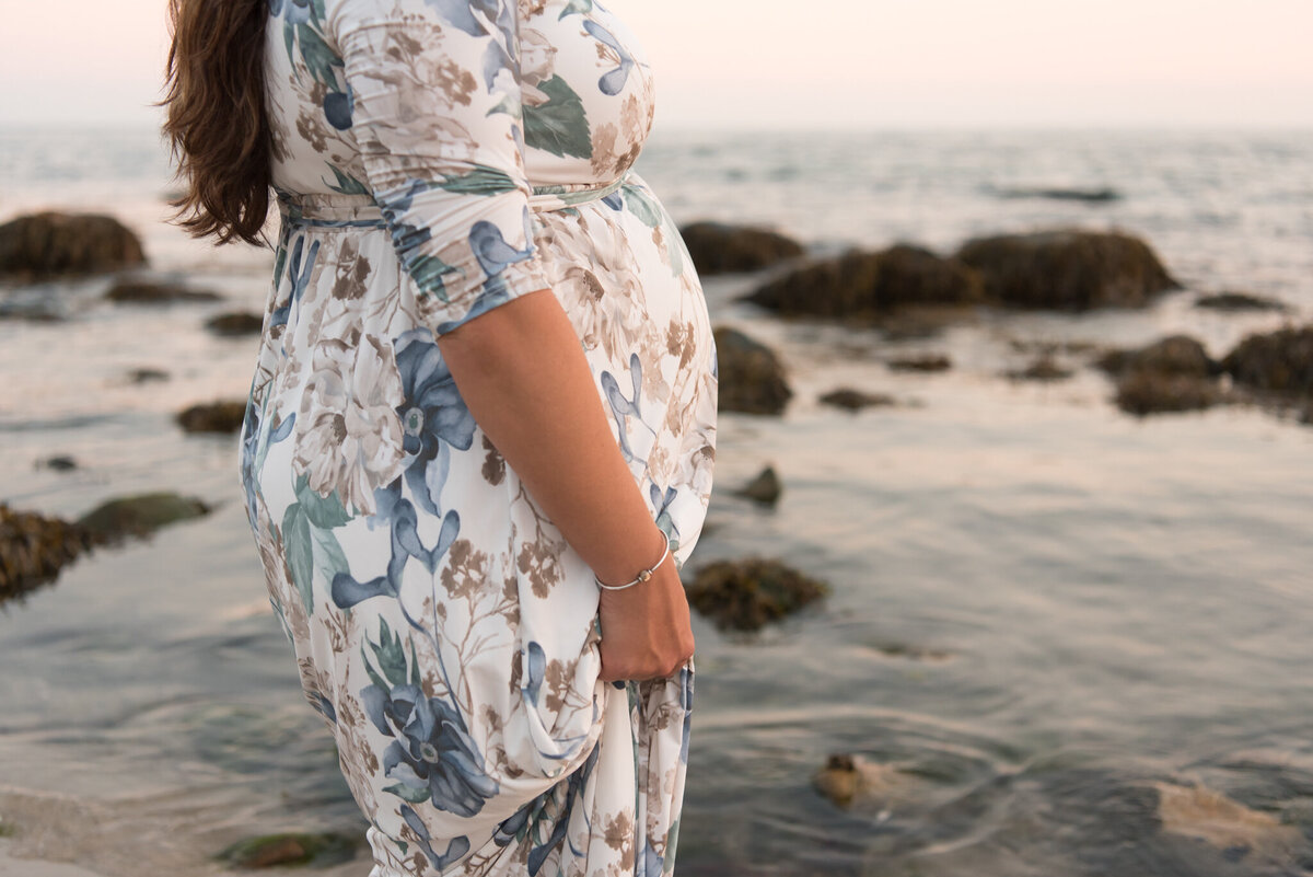 Pregnant mother looking out over the water in floral dress