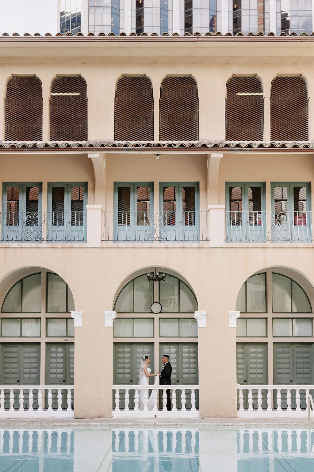 bride and groom facing each other under arches by the pool at cafe julia hawaii