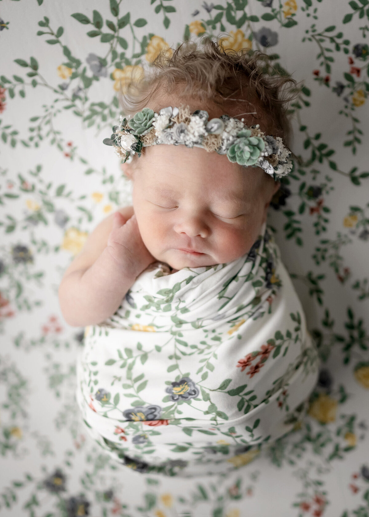 An image from a Pella Newborn Photography session of a baby girl sleeping in a floral print swaddle on matching bed with headband