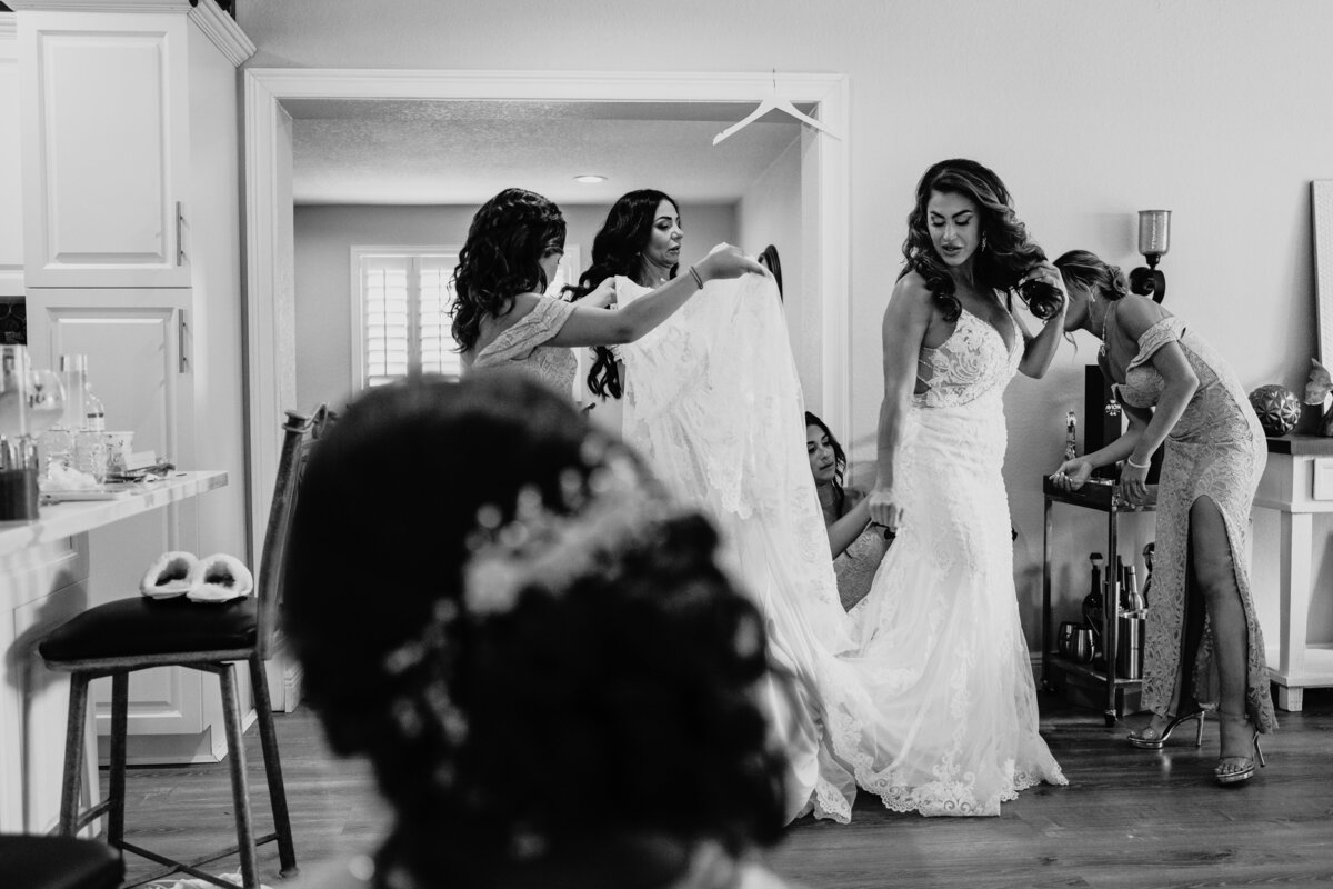 bride getting assistance from all her bridesmaids to get into her wedding dress before greek ceremony