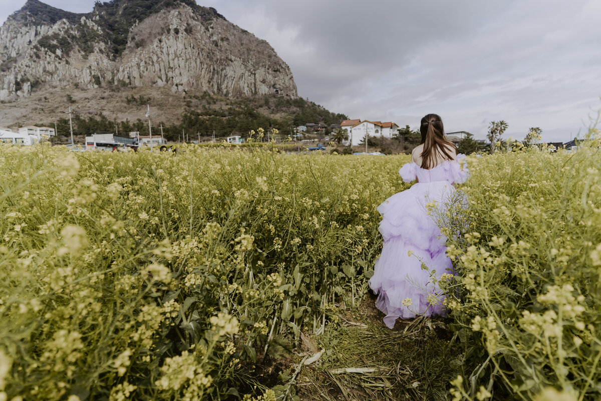 the bride walking in her favorite canola fields while wearing her raffled purple dress