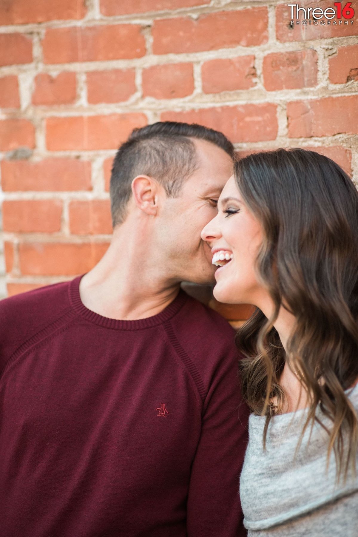 Groom to be whispers into his Bride's ear as she gives a big grin