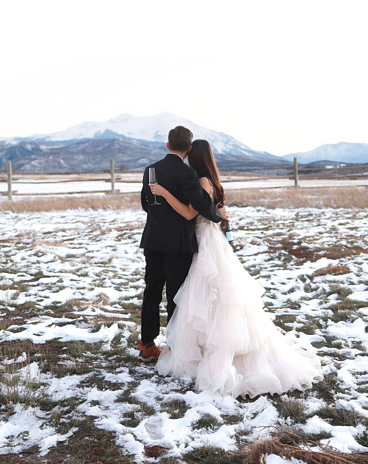 Gorgeous photo of a young bride and groom, embracing looking at the mountains together.