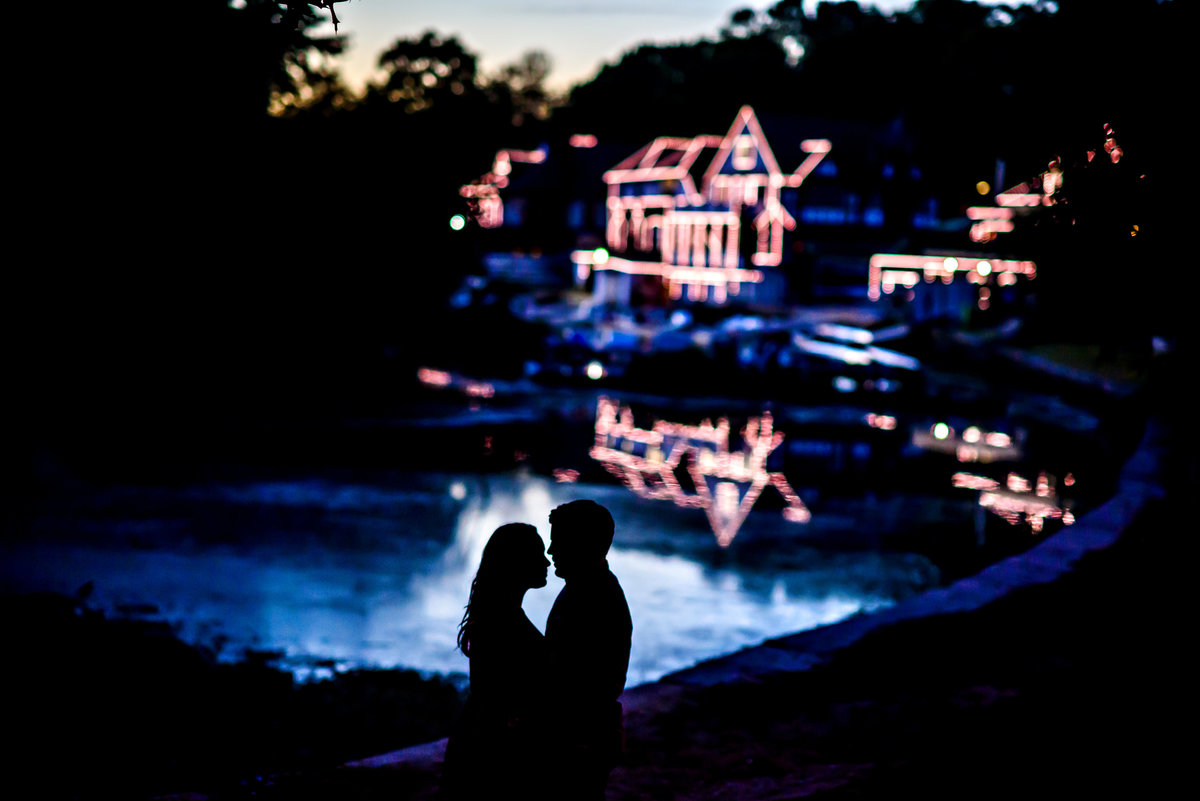 An engaged couple silhouetted in the water with boathouse row in the background.