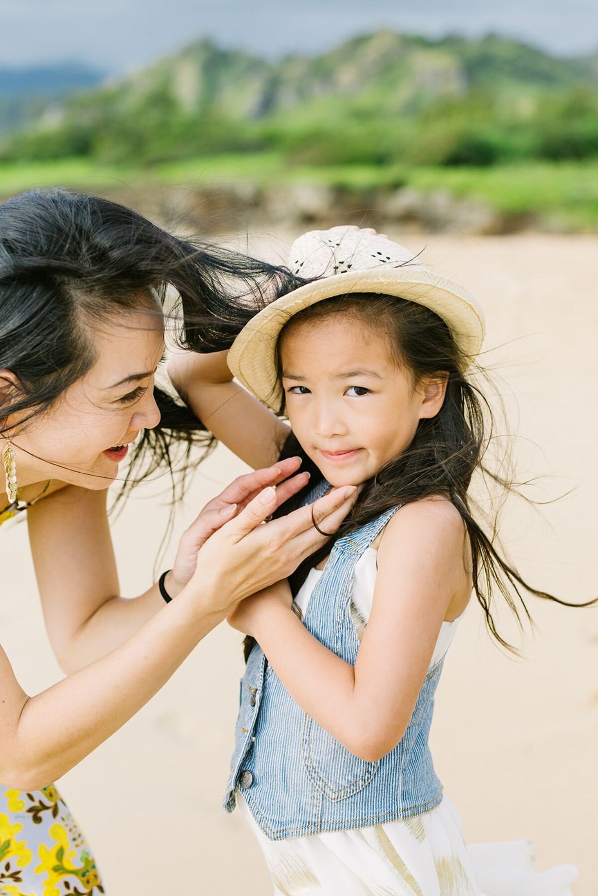 A mother leans into her daughter as the wind blows through the hair on the beach.