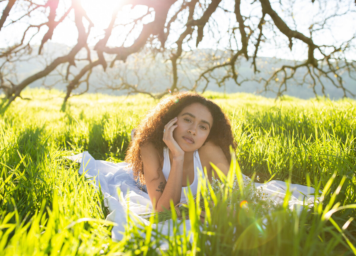 woman laying on the ground in a field resting her face on her hand