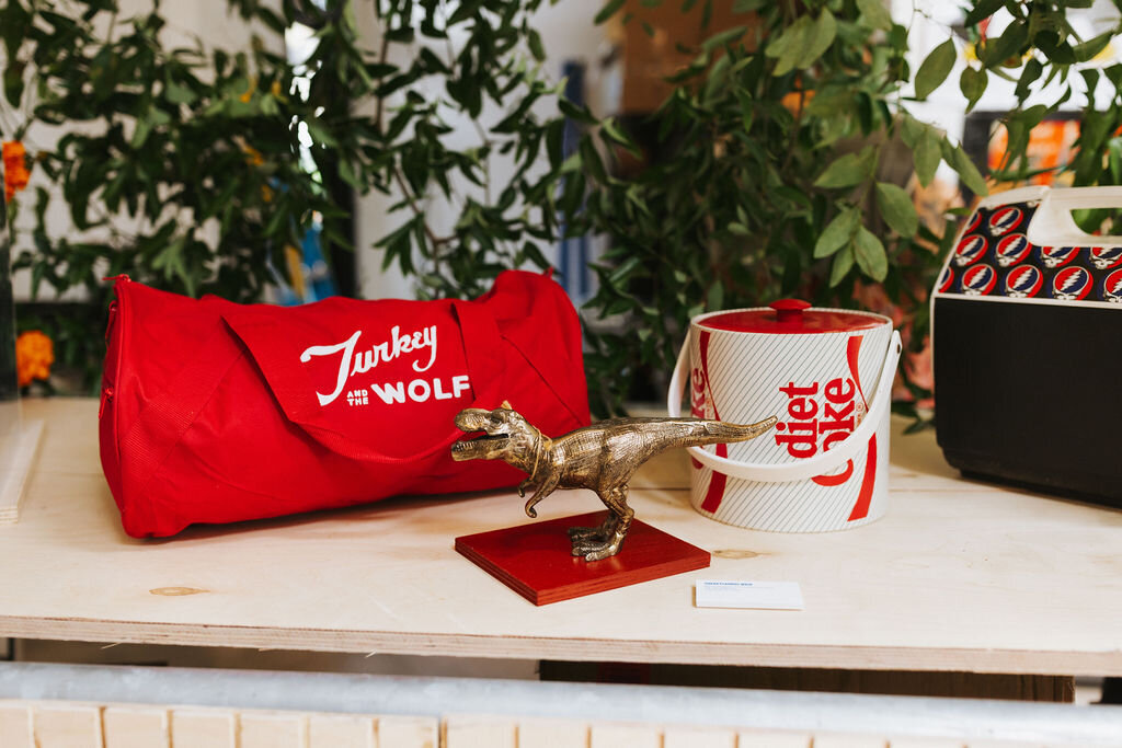 Display of Turkey and the Wolf collaboration items, including a red duffel bag and Coca-Cola mug, at the Absolut Vodka event.