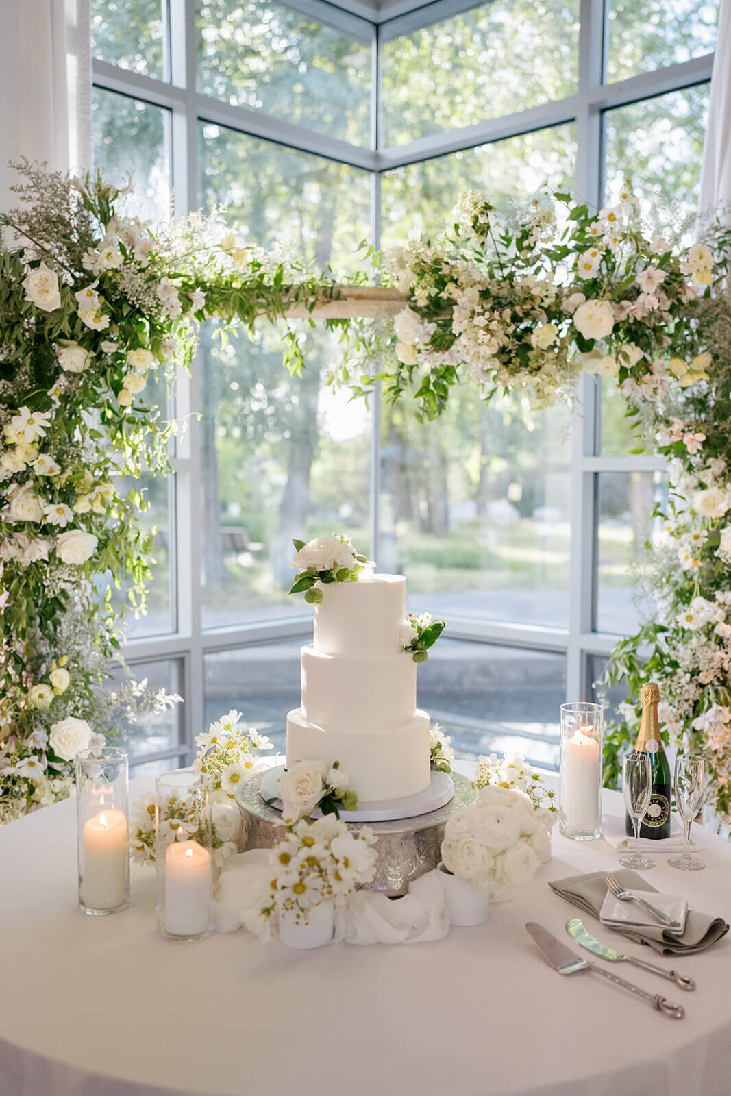 A beautiful white wedding cake adorned with simply elegant white florals and greenery sitting atop a cake table at the Aspen Meadows Resort wedding reception venue.