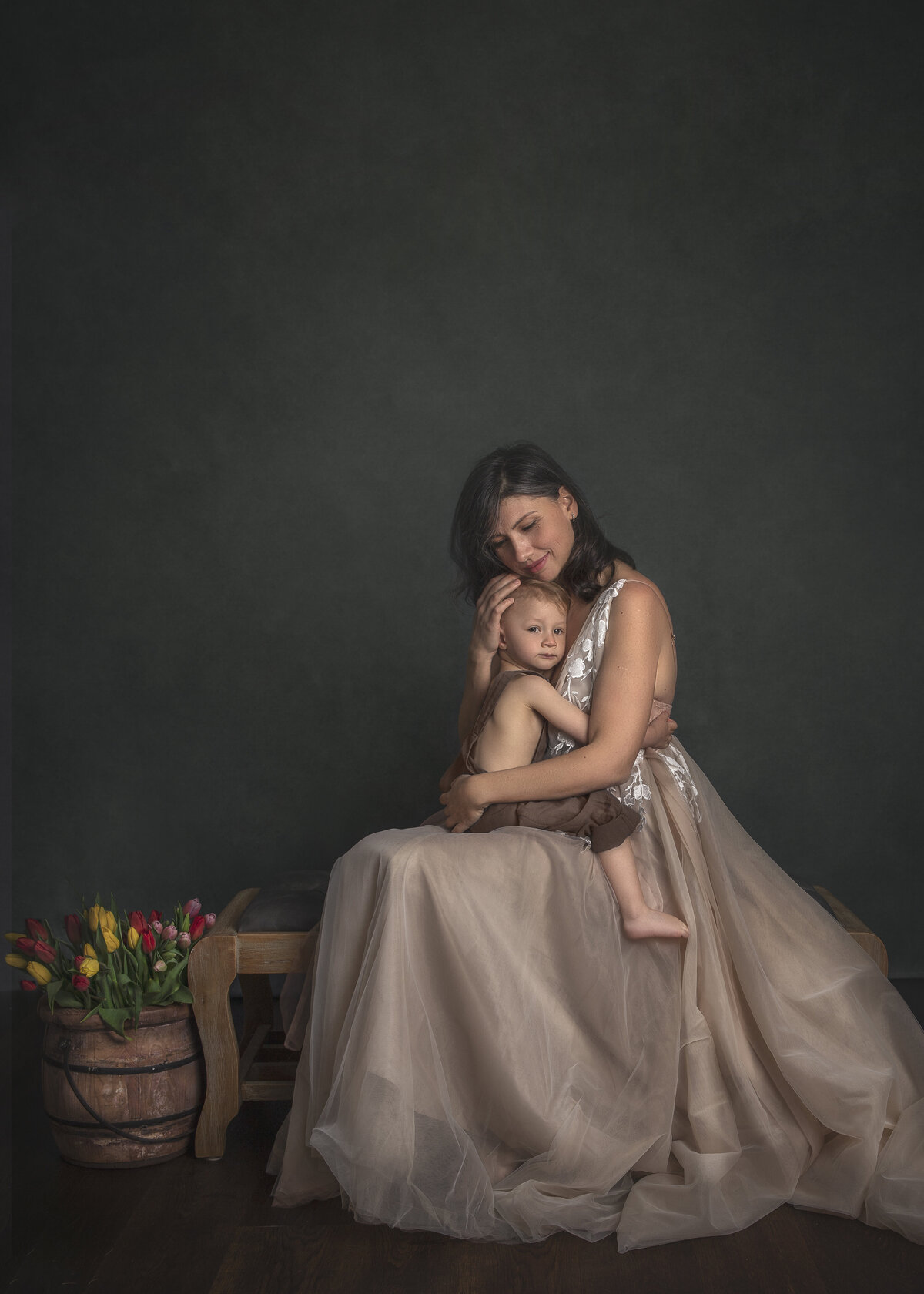 Mother cuddling her young son on a vintage heirloom bench, both dressed in stunning wardrobe pieces during a studio portrait session – Ottawa fine art family photography by Sonia Gourlie