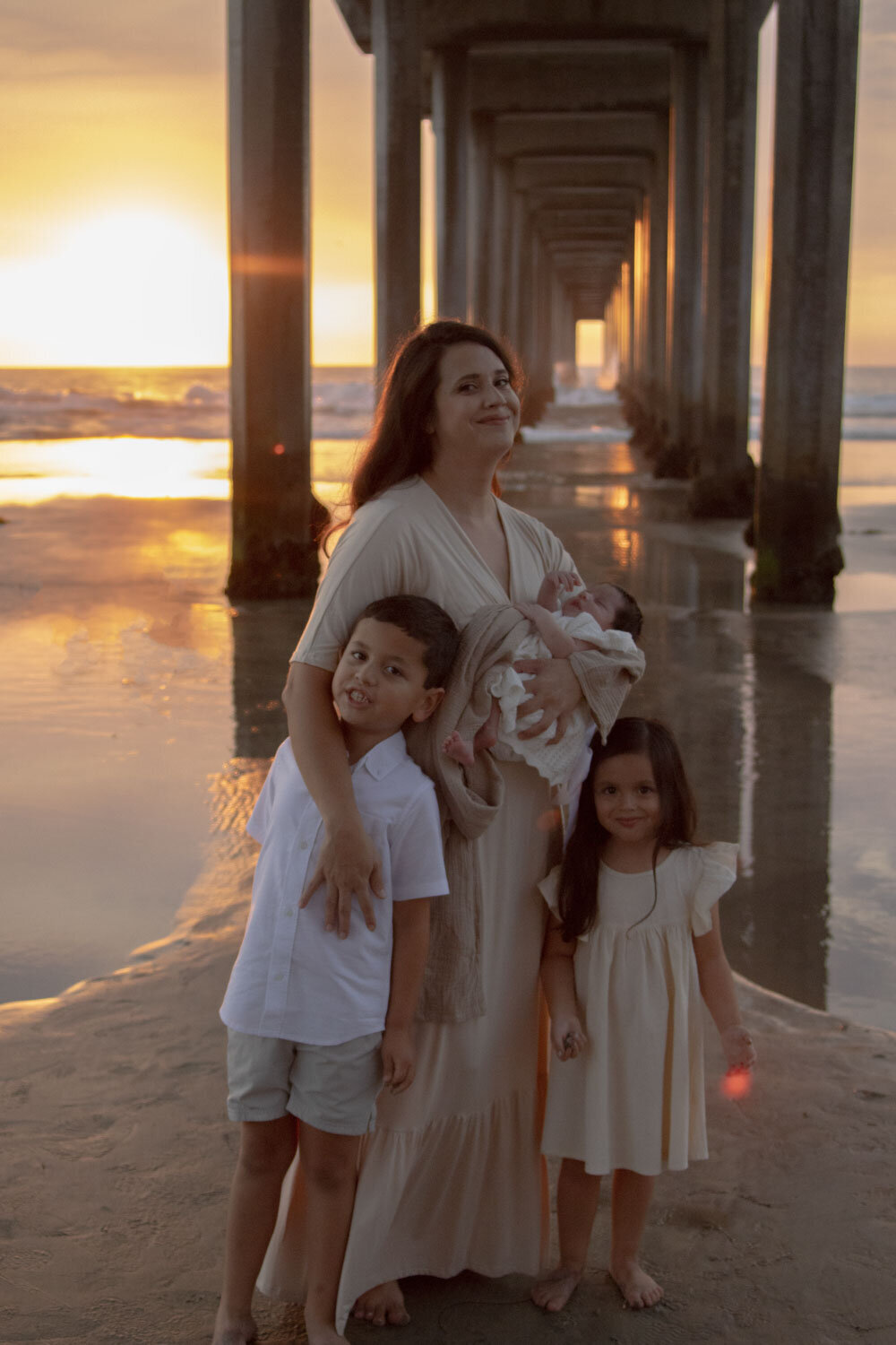 A mother and her two children standing on the beach at sunset