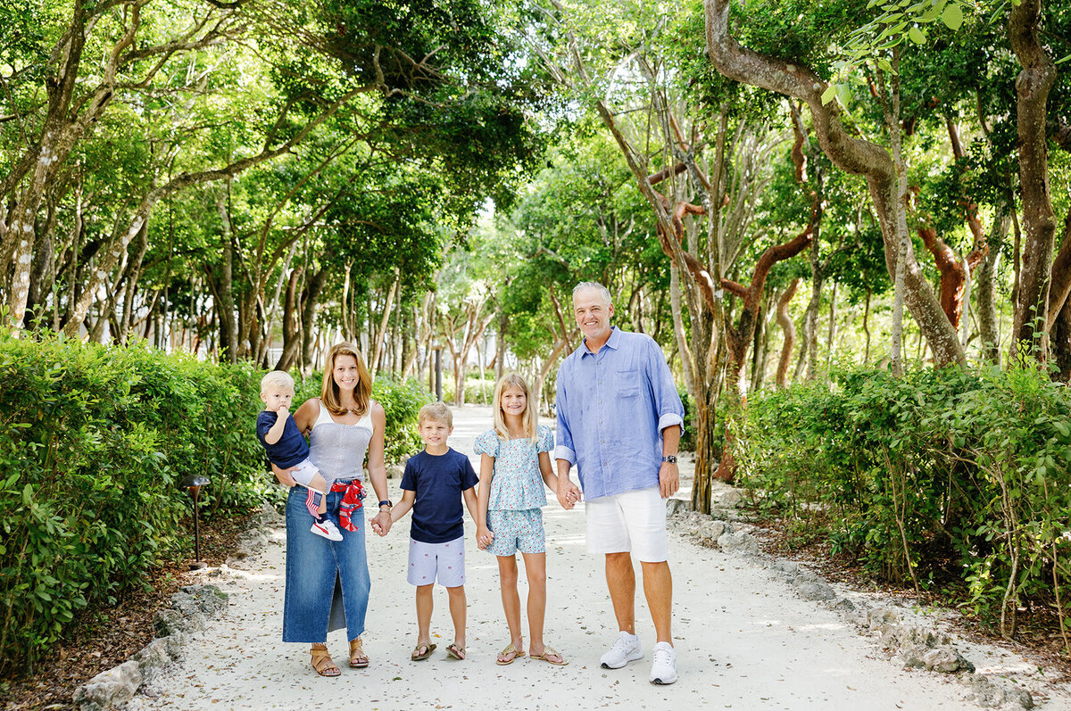 A family of five poses with American flags in front of lush greenery, capturing a heartfelt Florida Keys family portrait.