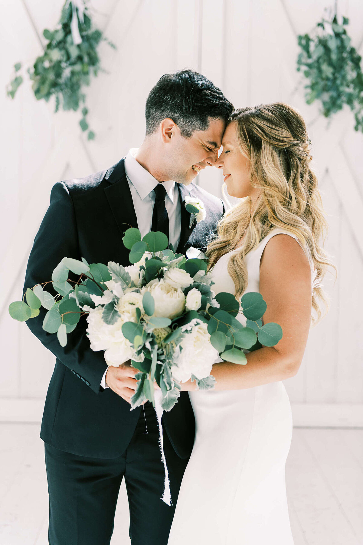 Newly married couple embraces while holding large greenery and floral bouquet at wedding