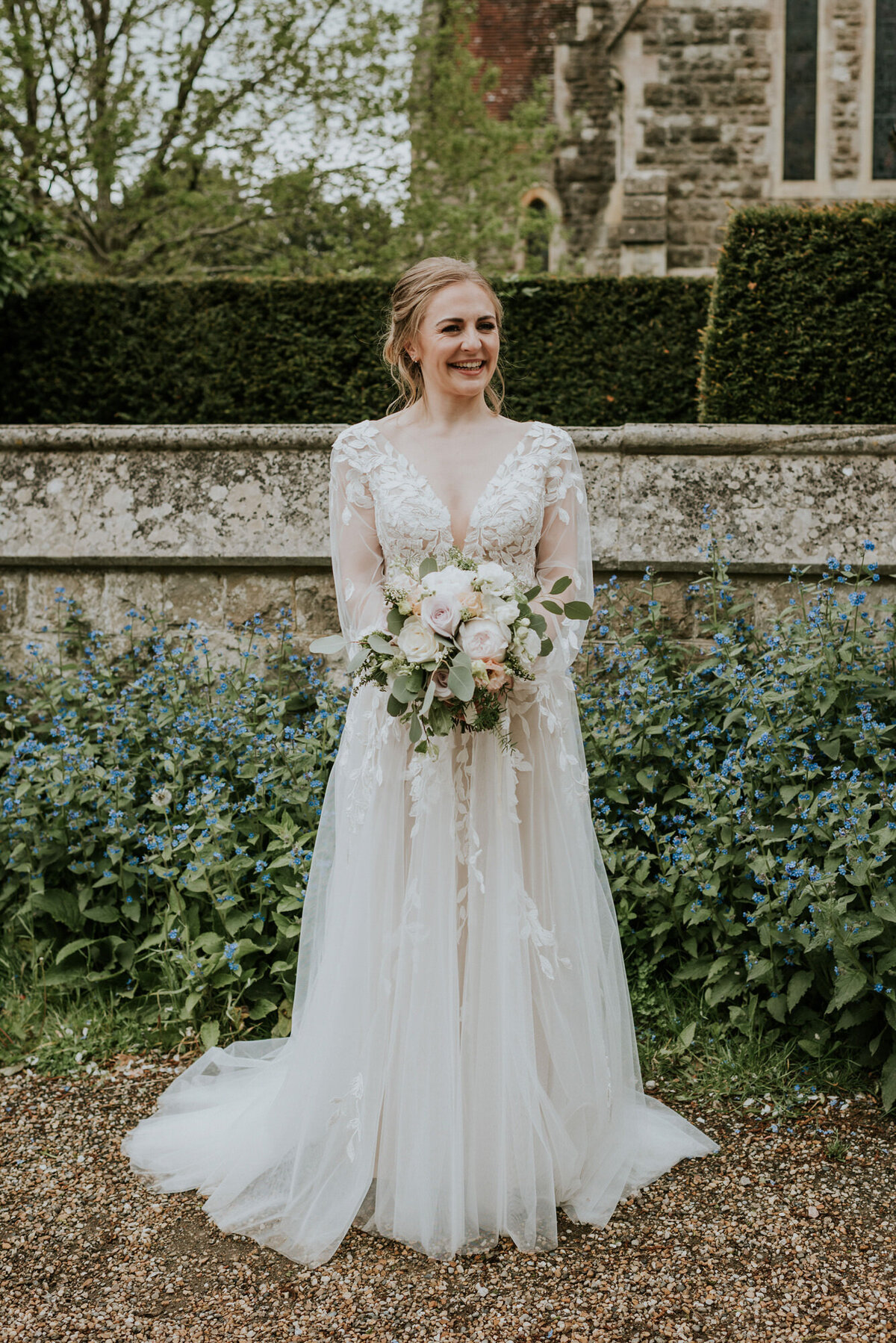 Bride standing outside church in front of blue flowers