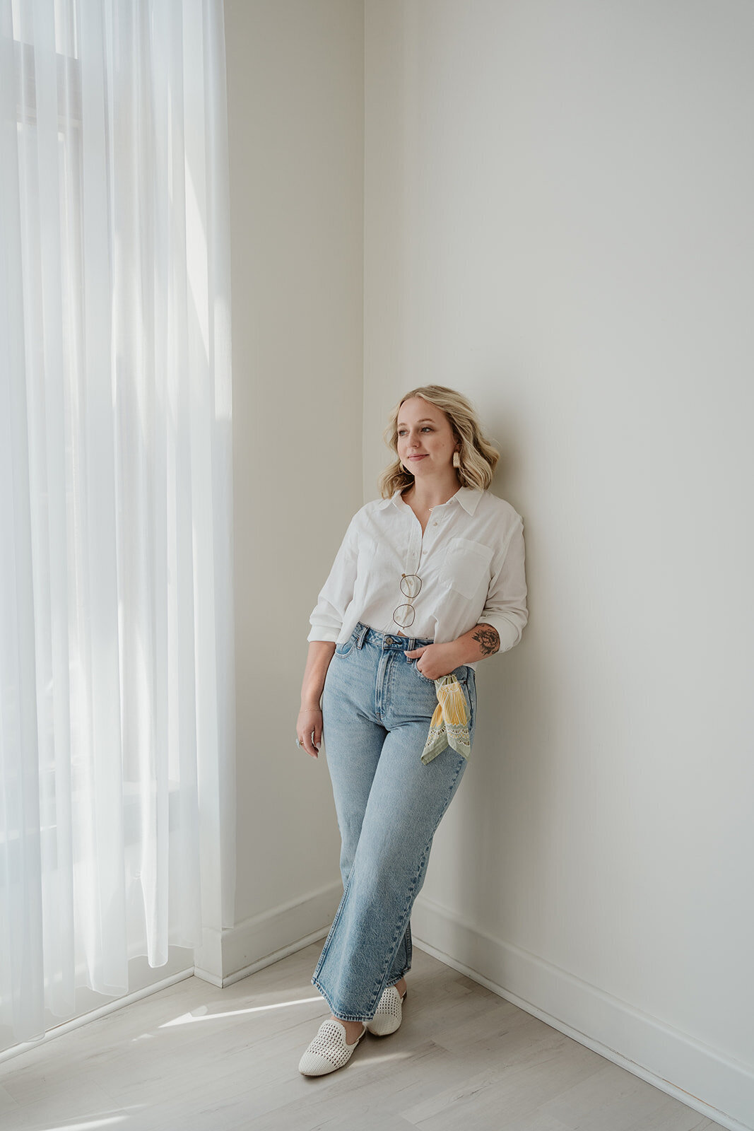 Full-body branding portrait of a woman leaning against a wall in natural light during a downtown Kalamazoo studio session.