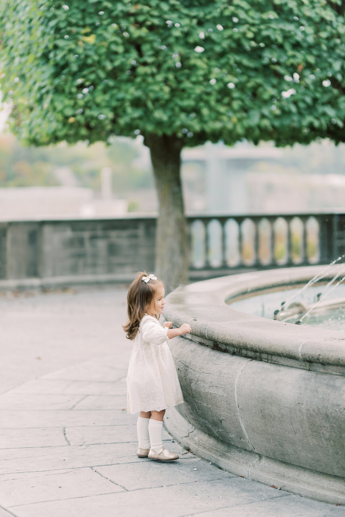 Young girl in white dress standing beside a stone fountain in Burlington, Ontario