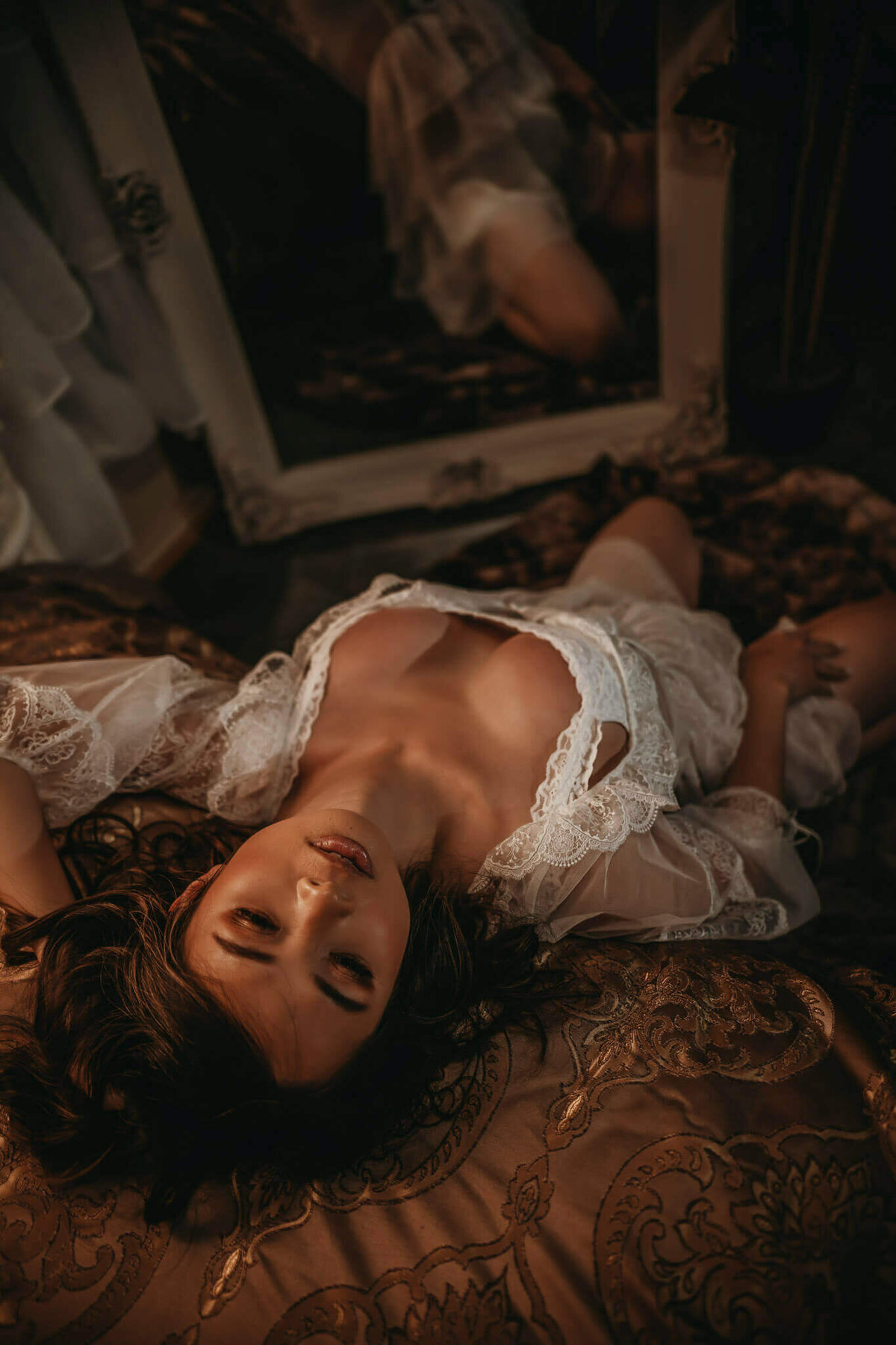 Woman in white lace robe leaning back on a bed in a DFW boudoir studio