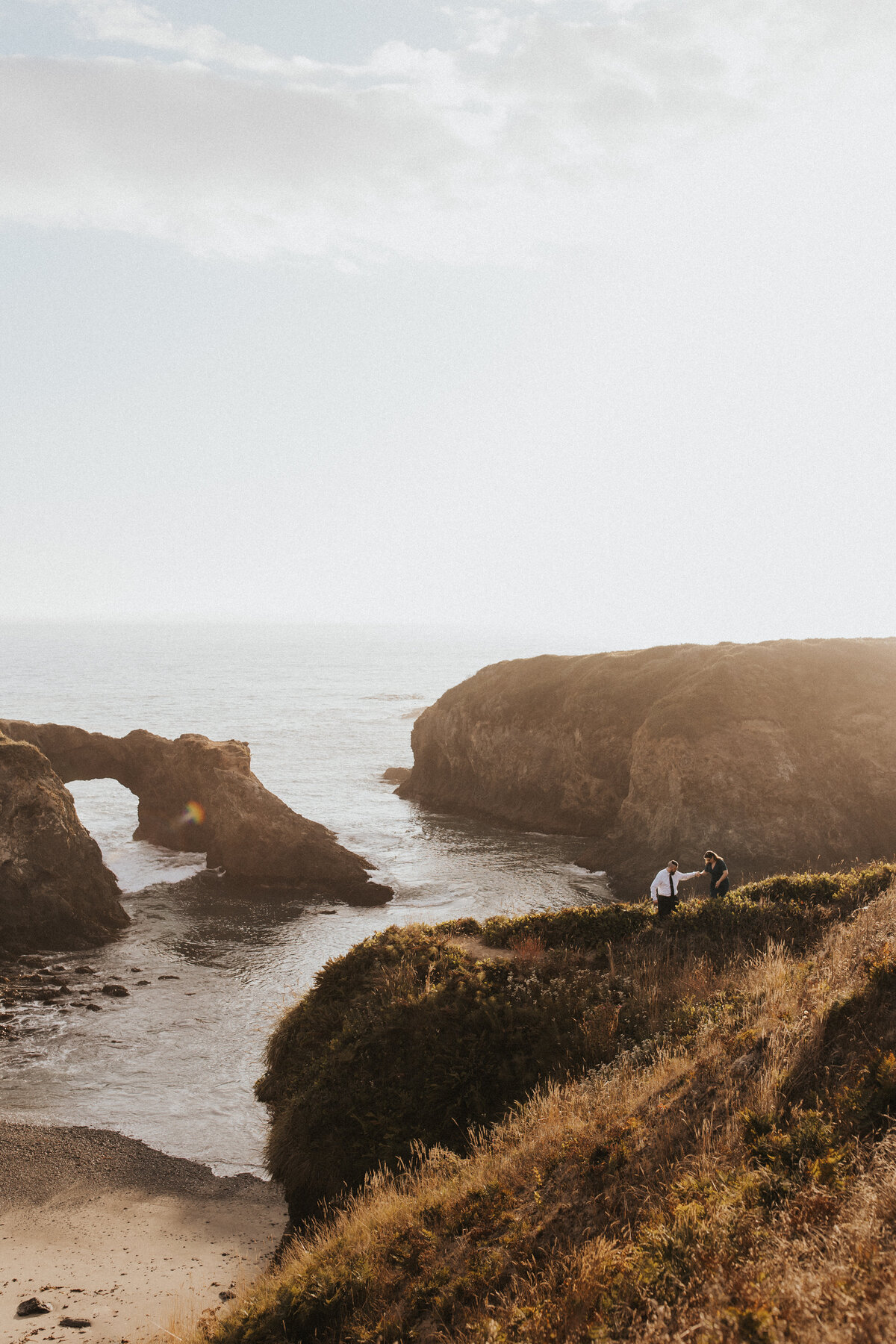 Documentary wedding photography capturing an intimate moment as a couple explores a dramatic coastline, bathed in warm sunlight, showcasing California's natural elegance.