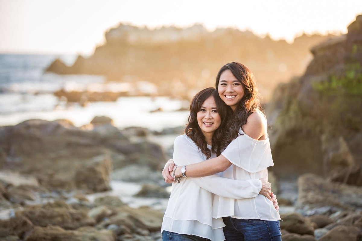 Mother and Daughter embrace one another as they smile for the family photographer on the rocky sands at the beach