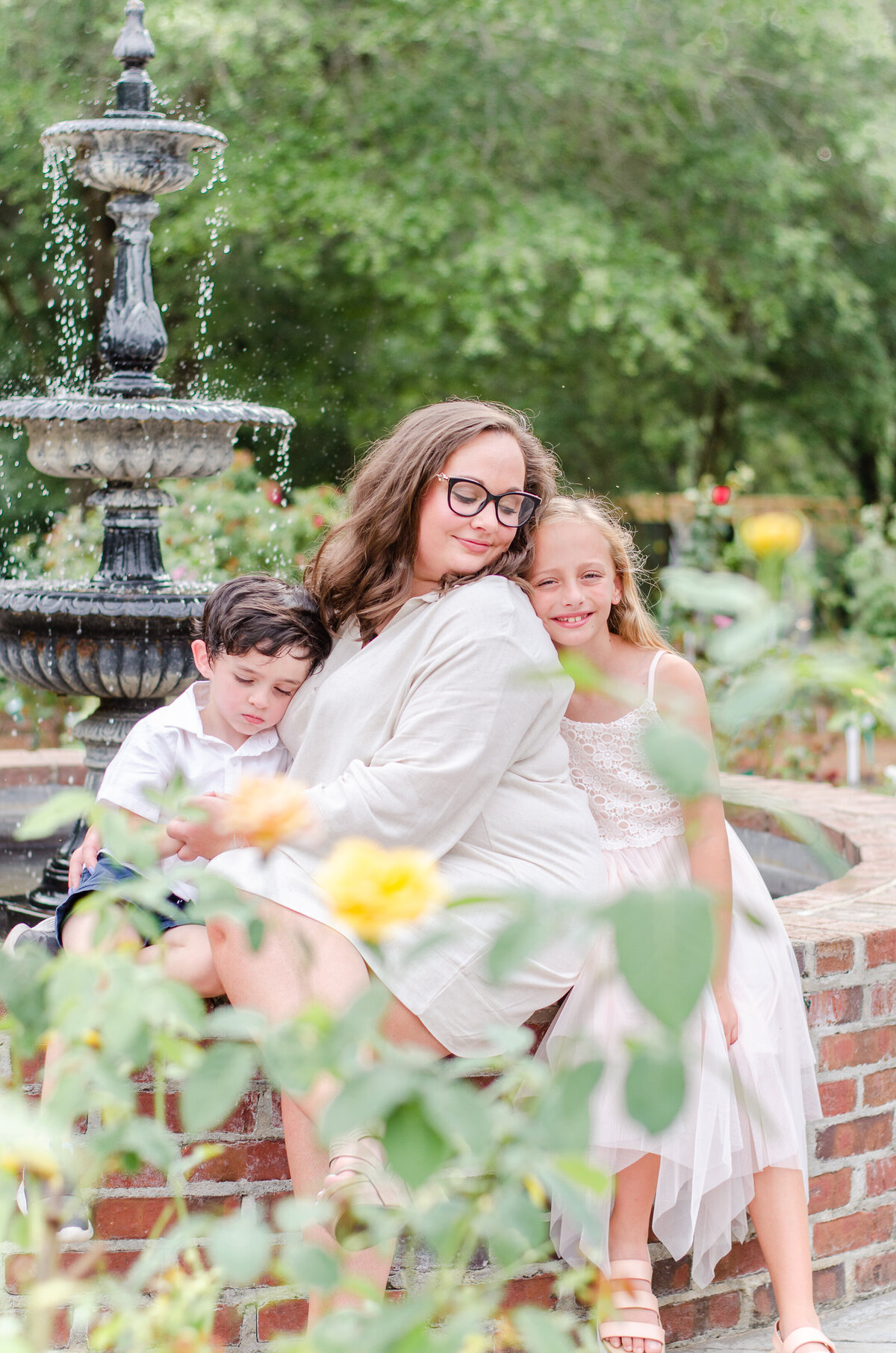 mother holds both her children close in a rose garden