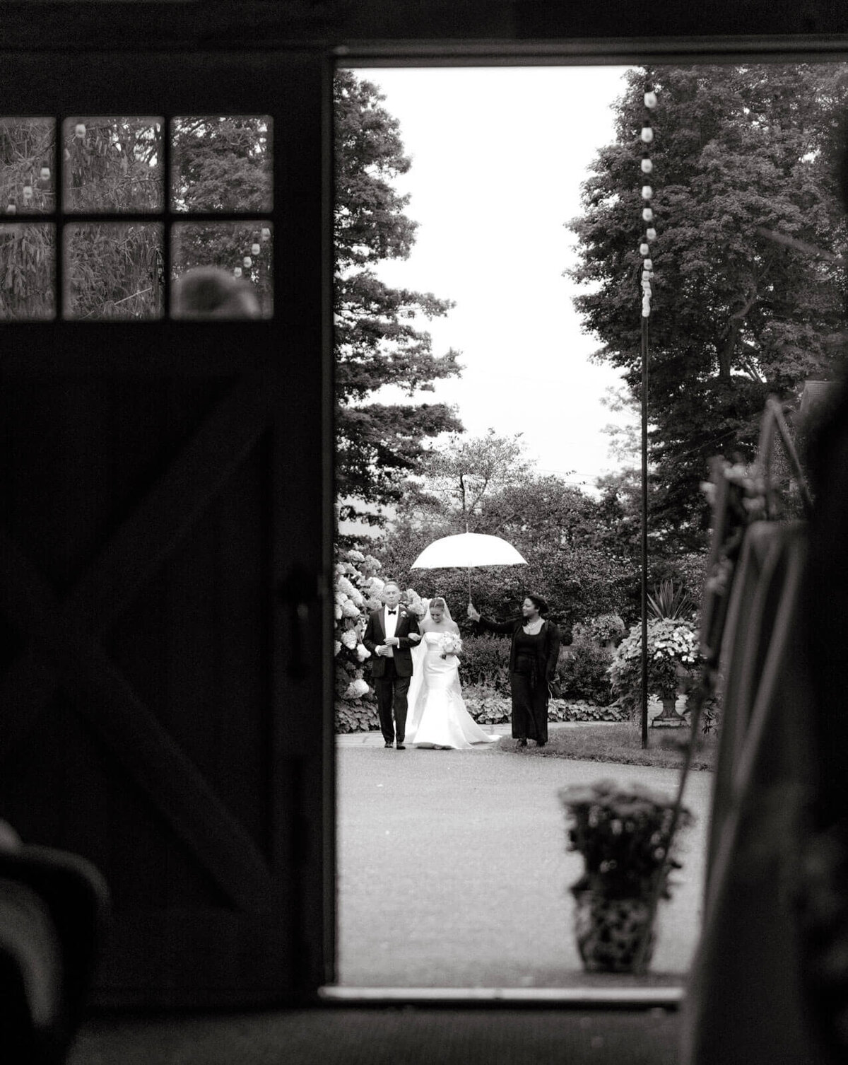 Escorted by her father, the bride is walking towards the wedding ceremony. A girl is holding a white umbrella for the bride.