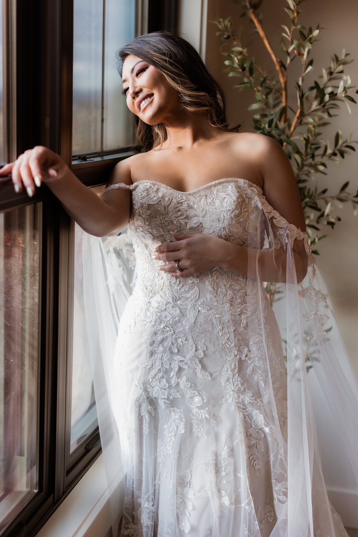 Asian bride smiling standing beside window.